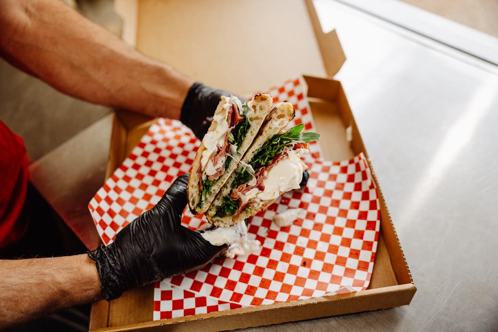 Fresh panino with prosciutto, rocket and creamy cheese held above a catering box