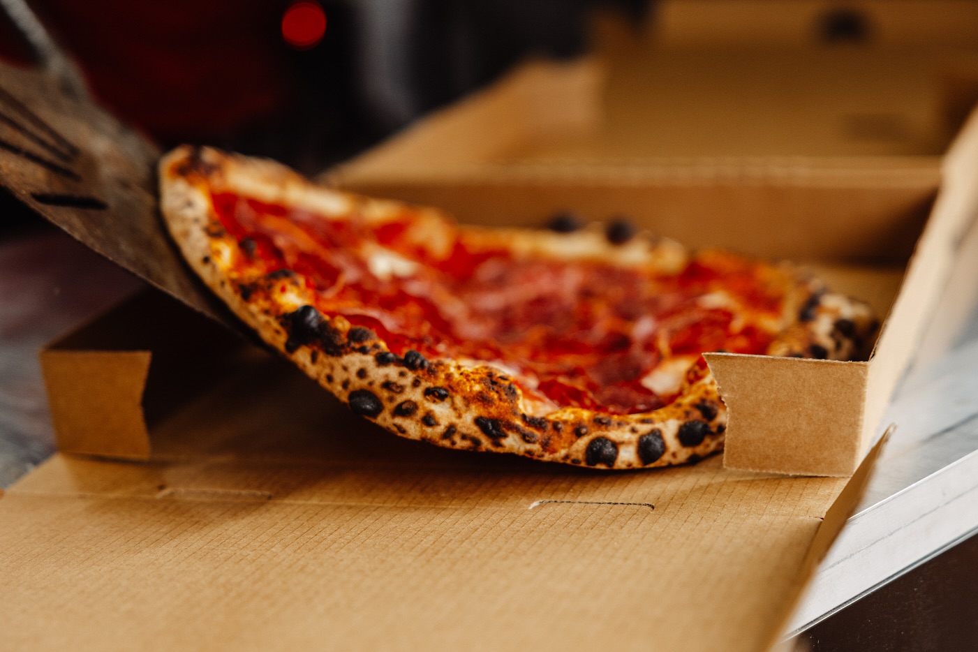 Woodfired salami pizza being placed into a takeaway box